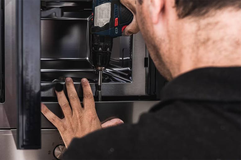 Appliance repairer technician placing a microwave to a kitchen cabinet.