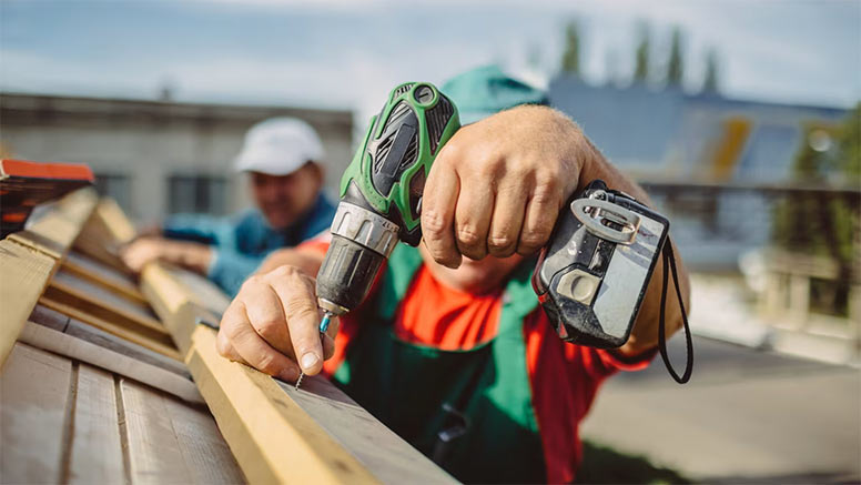 Roofer using a drill is fastening a cap to a new house roof.
