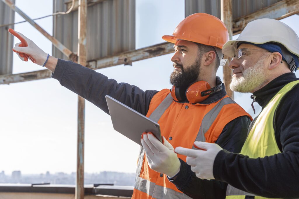 Two construction workers in safety gear on-site using a tablet to review plans.