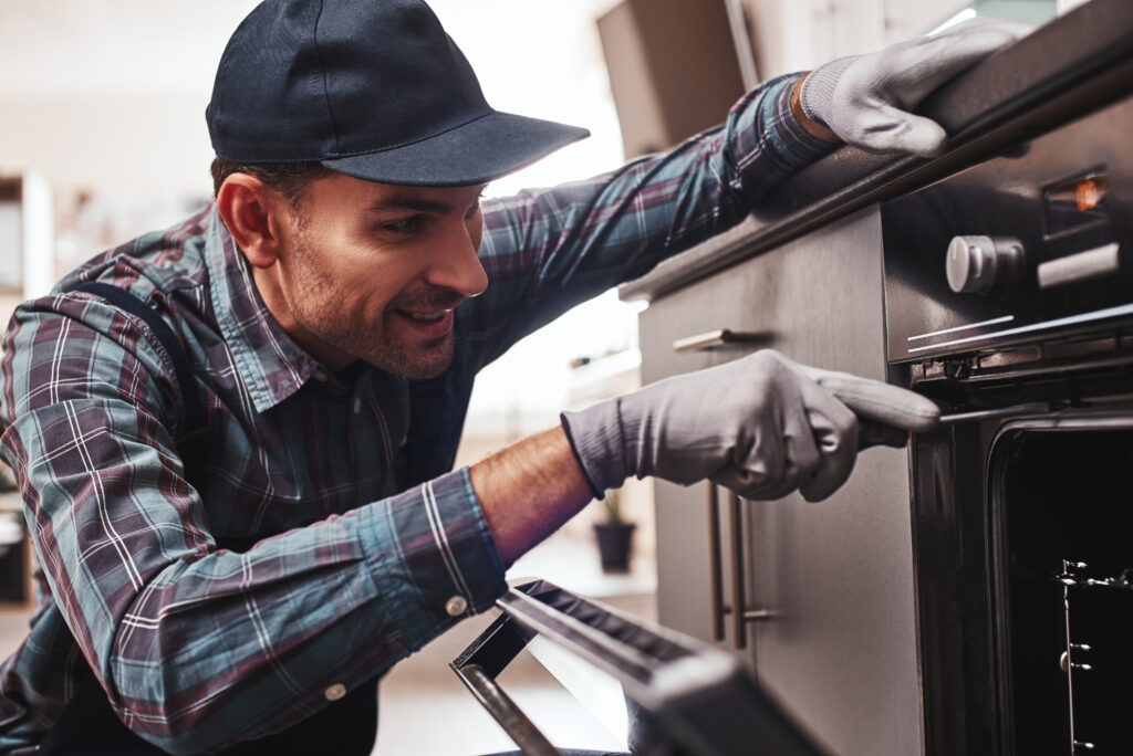 Don't delay with repair. Close-up of repairman examining oven with screwdriver in kitchen with tool case