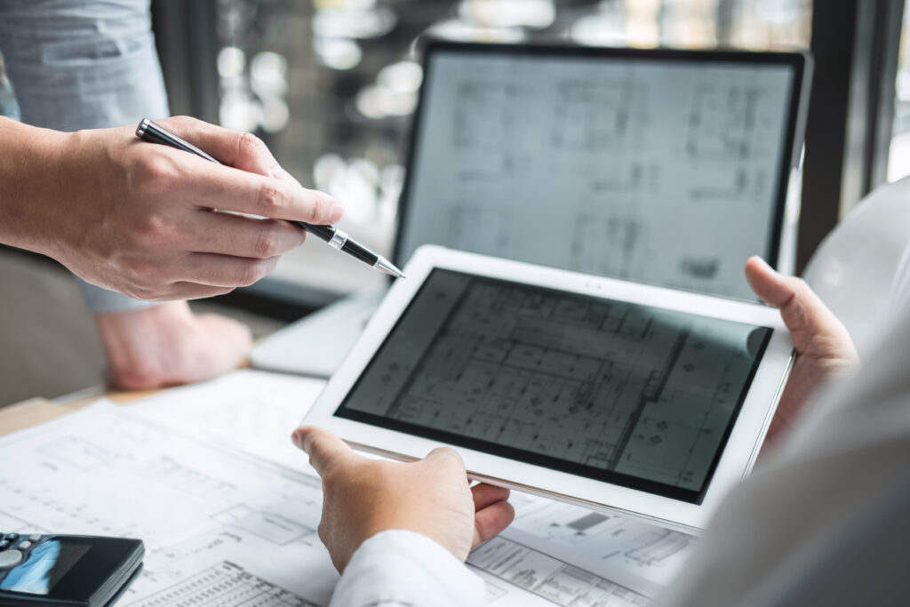Construction professionals reviewing digital blueprints on a tablet surrounded by paper plans.