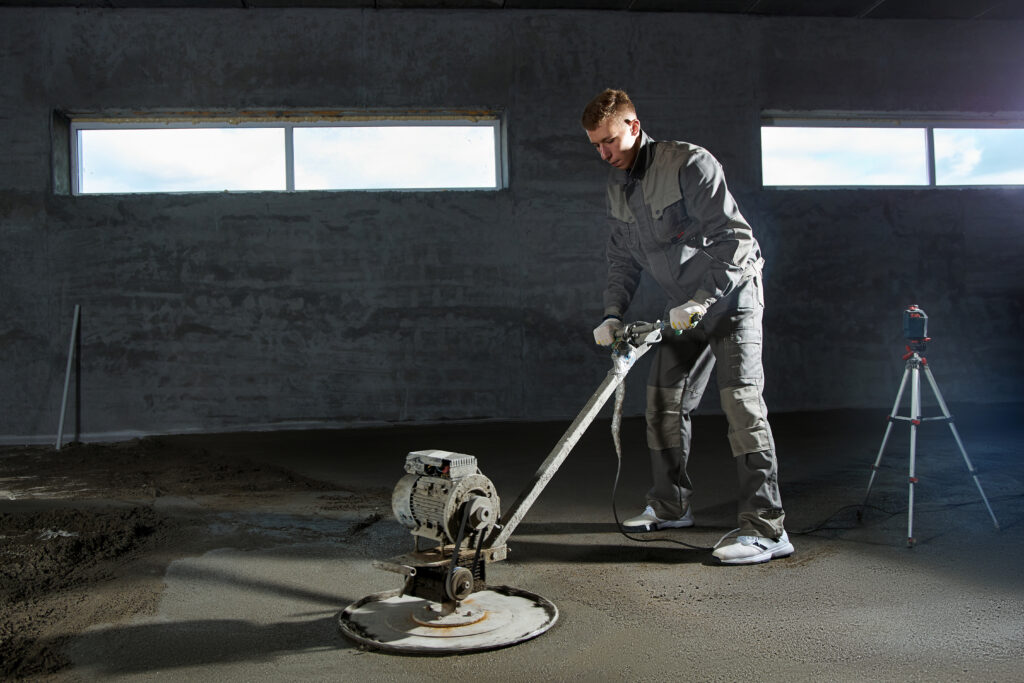 Construction worker filling and leveling the floor with concrete. Smooth floors made of a mixture of cement, industrial concreting.