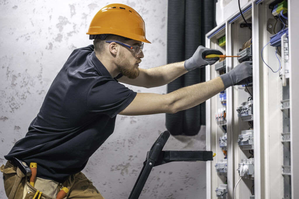 Electrician using an insulated screwdriver to work on a circuit panel.