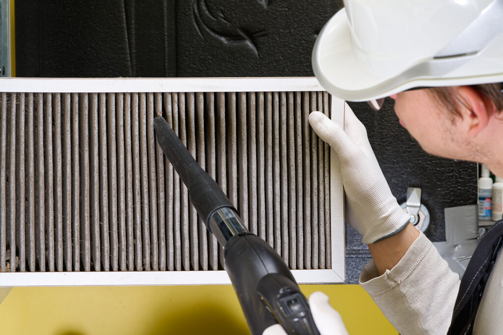 Close-up of a technician vacuuming a dirty HVAC filter.