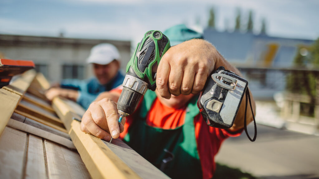 Roofer using a drill is fastening a cap to a new house roof.