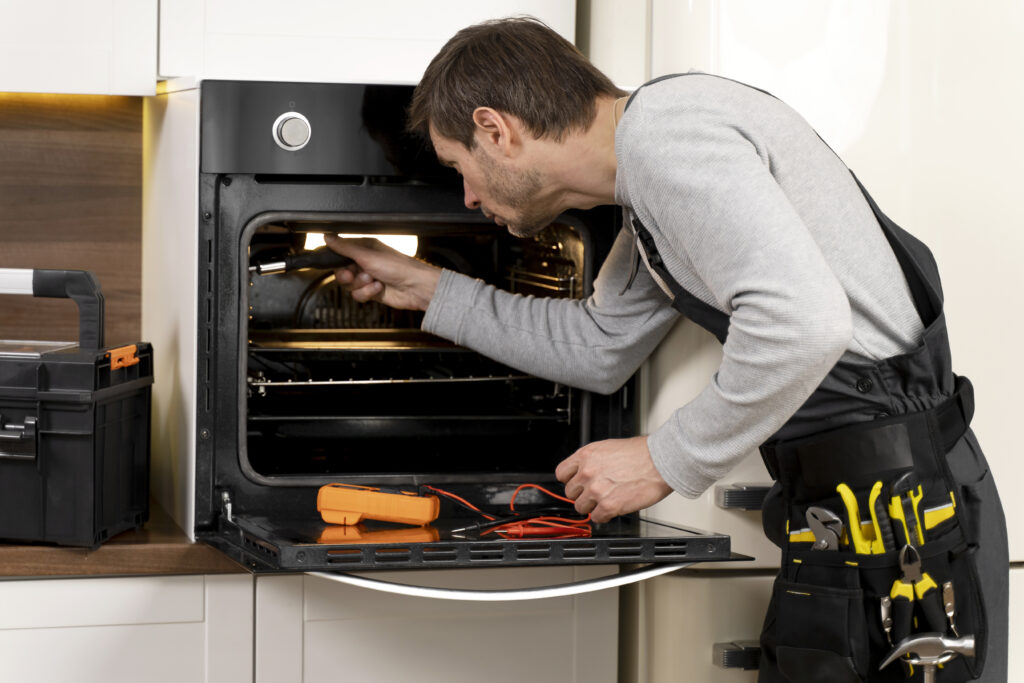Appliance repair worker is fixing an oven with a screwdriver.