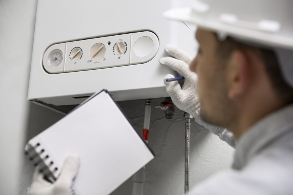 HVAC technician inspecting a boiler or water heater while taking notes for a service report