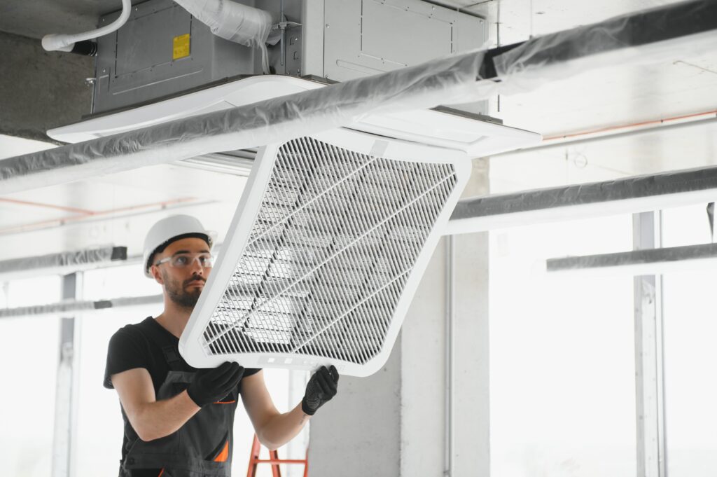 Technician installing or servicing a ceiling-mounted air conditioning system in a modern building.