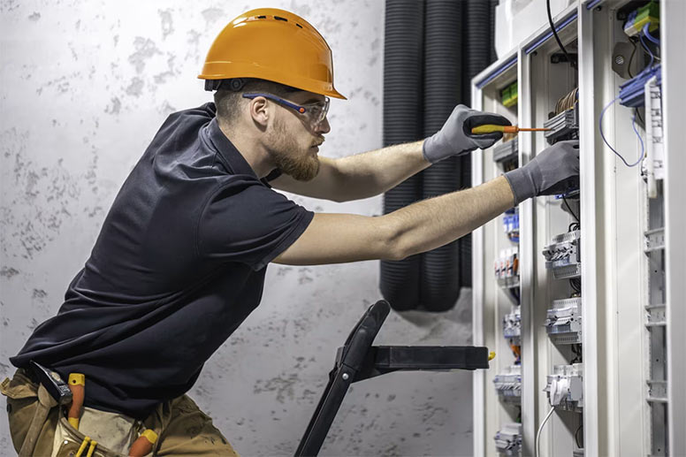 Electrician using an insulated screwdriver to work on a circuit panel.