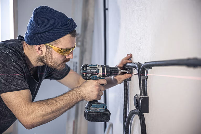 HVAC technician using a power drill to install flexible conduit on an interior wall.