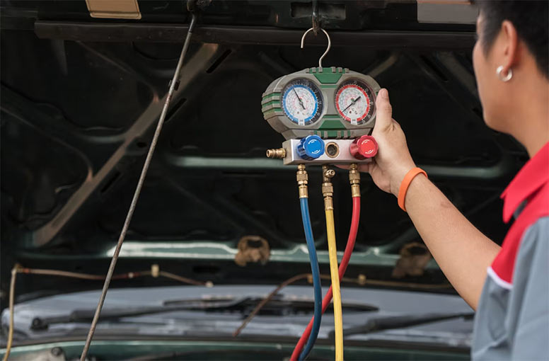 HVAC technician holding a manifold gauge set to measure refrigerant pressure on a vehicle air conditioning system.