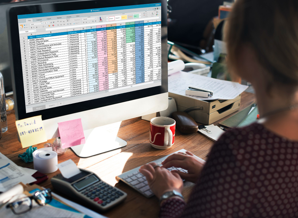 Business professional reviewing a spreadsheet of inventory and receivables on a desktop monitor.