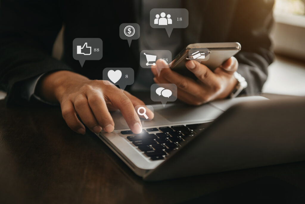 Person using a laptop and mobile phone with social media and digital marketing icons floating above
