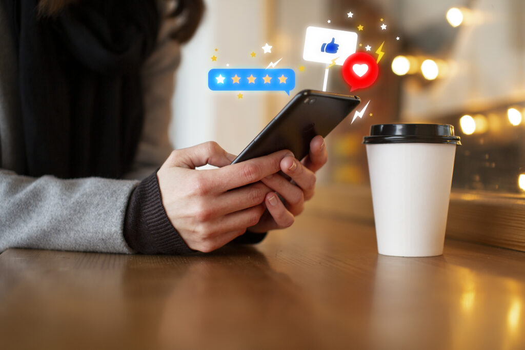 Person holding a smartphone with digital icons for reviews and likes, symbolizing online engagement and customer feedback.