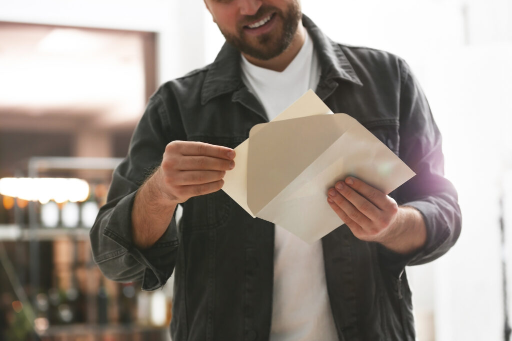 Man smiling while opening a paper envelope indoors.