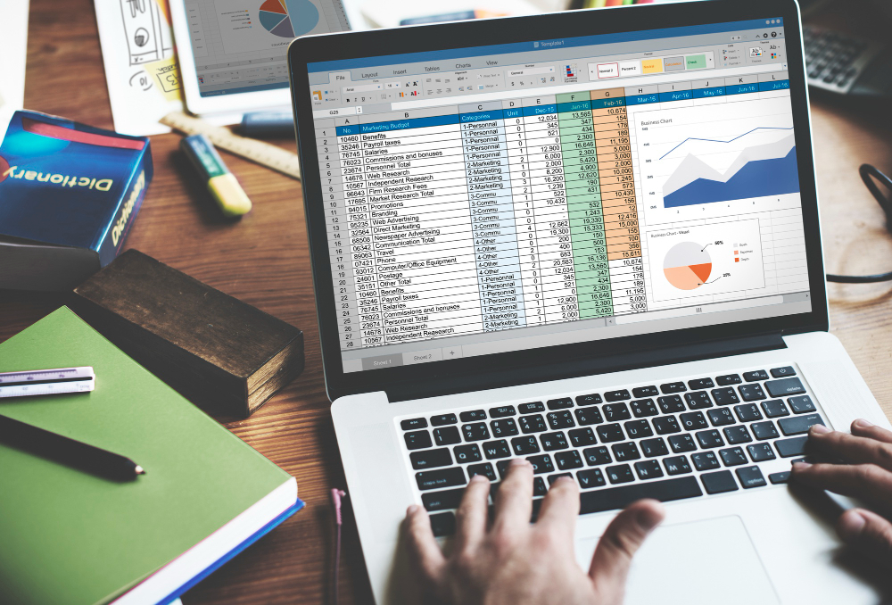 Closeup of hands entering journal entries on a laptop with financial analysis charts on screen.