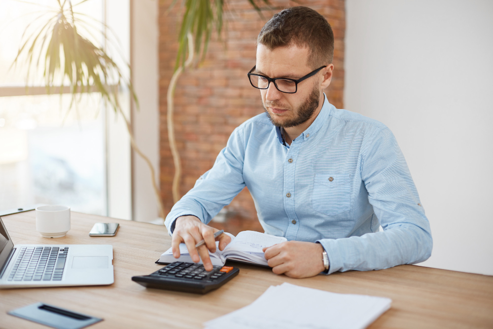 Business owner analyzing retained earnings on financial statements with calculator