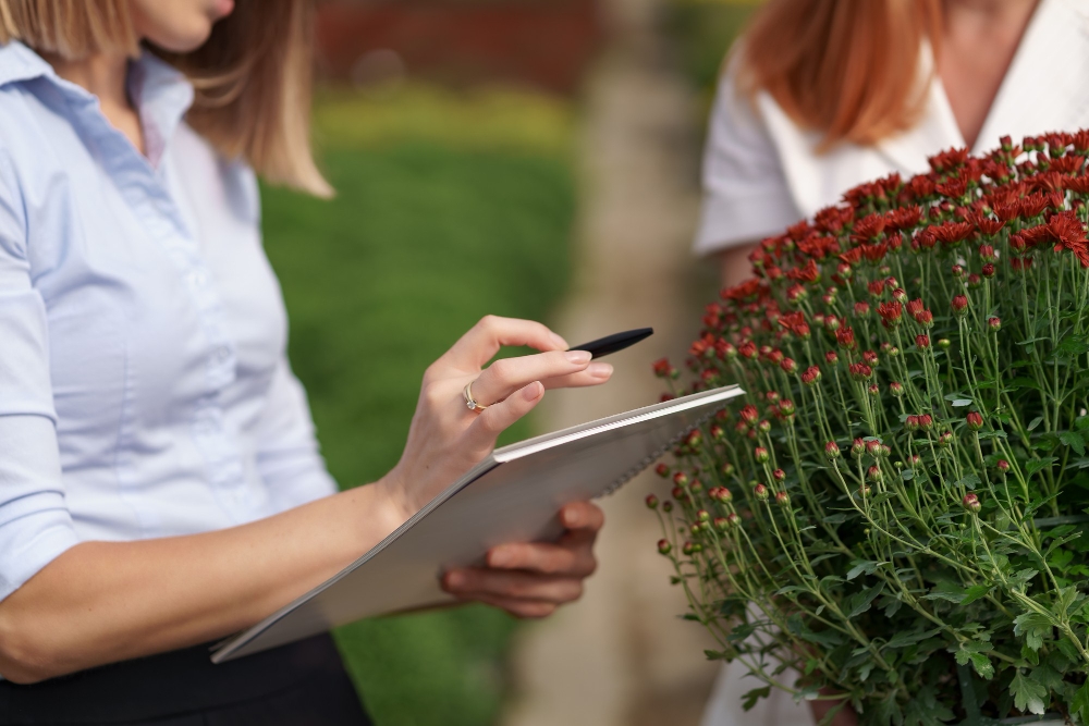 Greenhouse owner presenting flowers to a customer, illustrating staff training and client relationship building in landscaping.