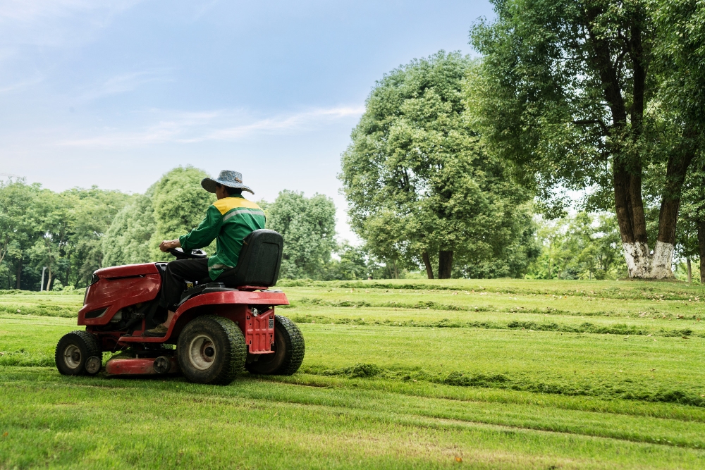 Worker driving a red riding lawn mower on a large green lawn, showing landscaping equipment and business expenses.