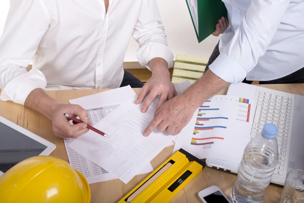 Two construction managers reviewing cost charts and spreadsheets, highlighting operating expenses in construction projects.