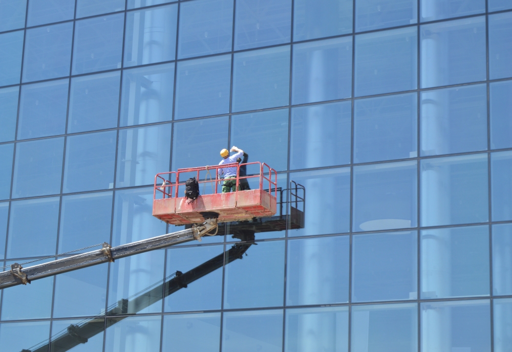 Two workers on a lift cleaning large glass windows of a high-rise building.