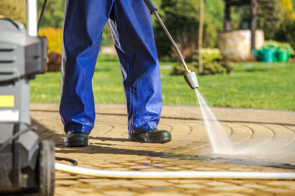 Contractor pressure washing roof gutters with safety equipment, representing house exterior cleaning.