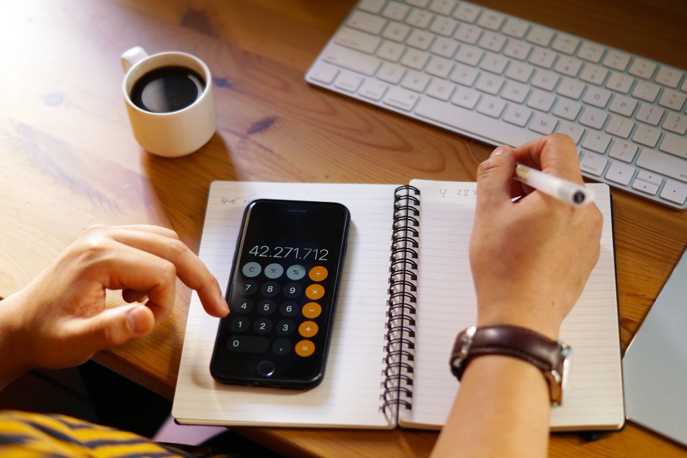 Entrepreneur calculating work hours with laptop and calculator, representing PTO and overtime adjustments.