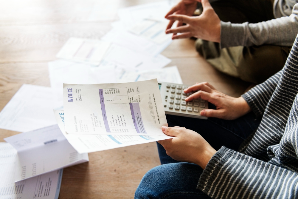 Freelancers reviewing invoices with a calculator and paperwork, managing finances with Google Docs templates.