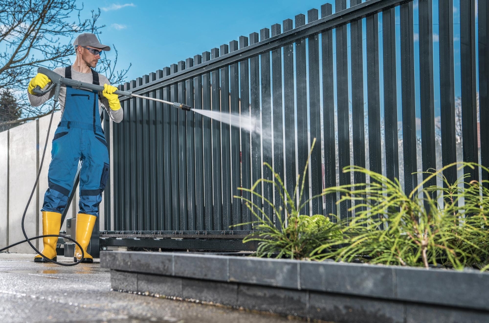 Worker cleaning a metal fence with pressure washer.