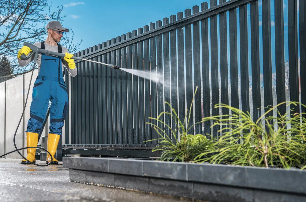 Worker cleaning a metal fence with pressure washer.