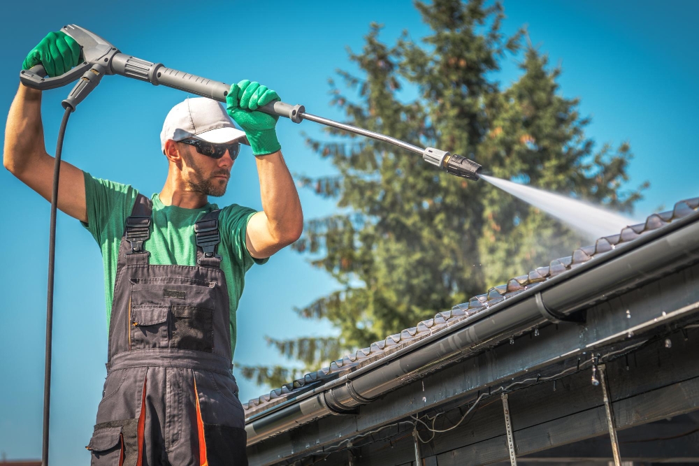 Worker pressure washing wooden fence with water spray, showing cleaning siding and outdoor wood surfaces.