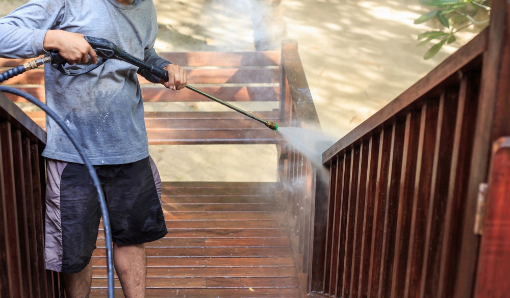 Worker pressure washing wooden stairs with high-pressure water stream, showing how to clean outdoor surfaces.