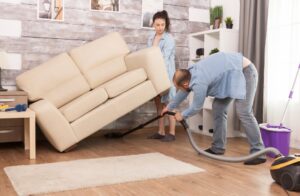 Couple vacuuming and lifting sofa during home cleaning