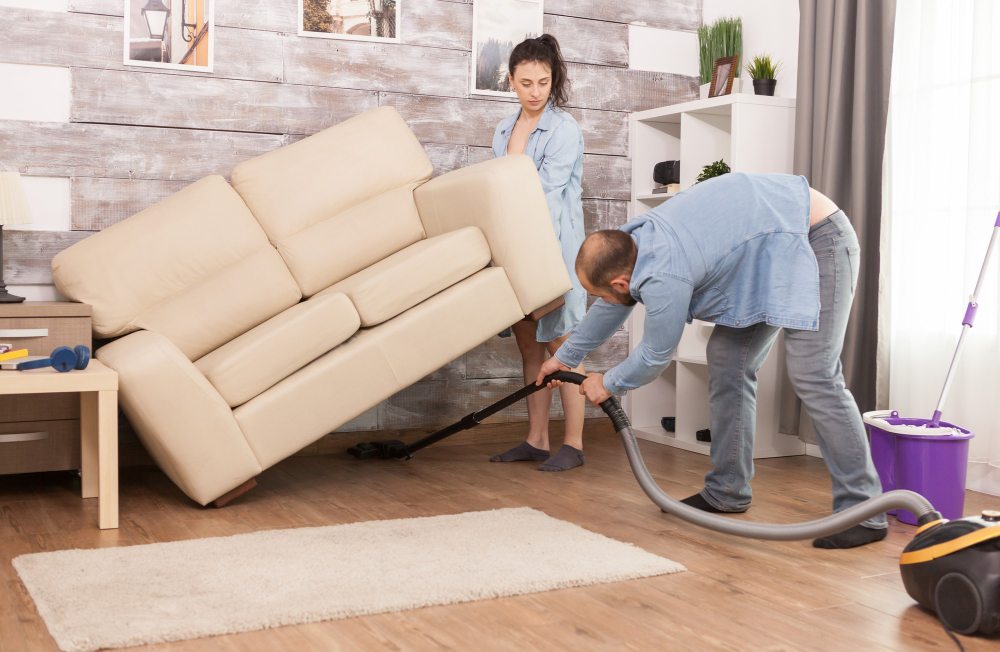 Couple vacuuming and lifting sofa during home cleaning