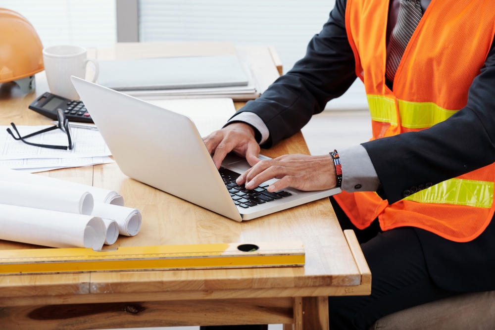 Contractor in safety vest using laptop to manage projects