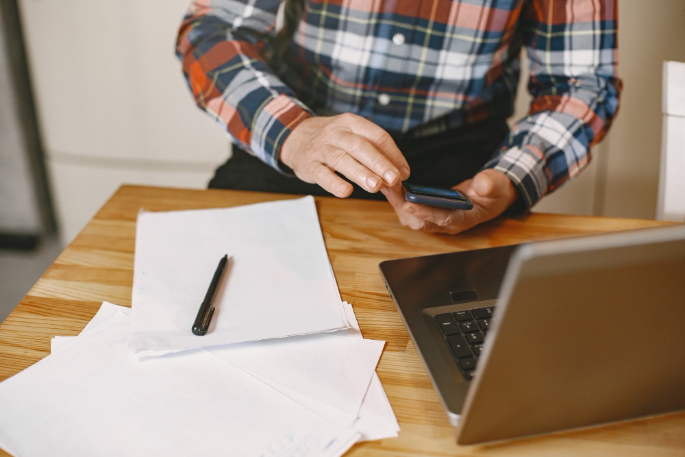 Senior man using laptop and phone to manage billing tasks