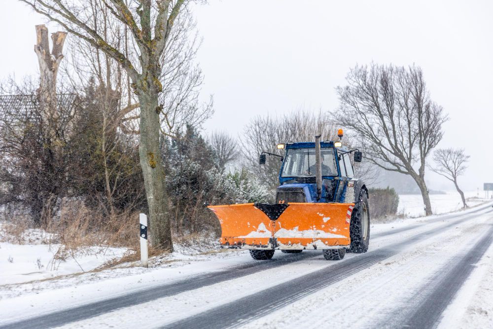 Snow removal tractor clearing snow from rural roadway