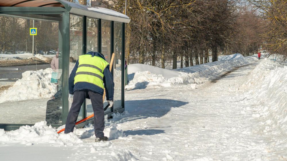 Worker shoveling snow from icy sidewalk during winter