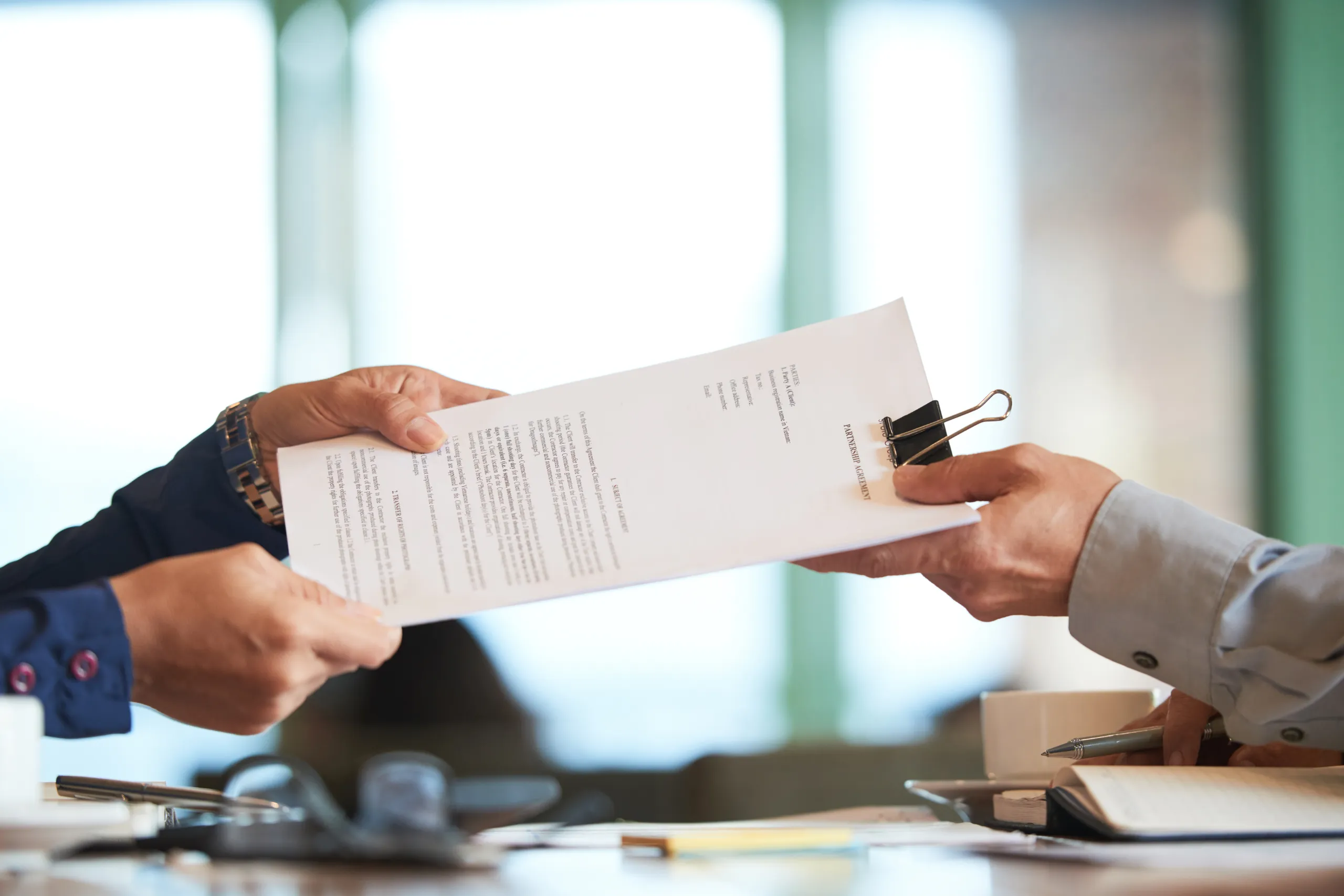 Close-up of hands passing a signed contract between two people.