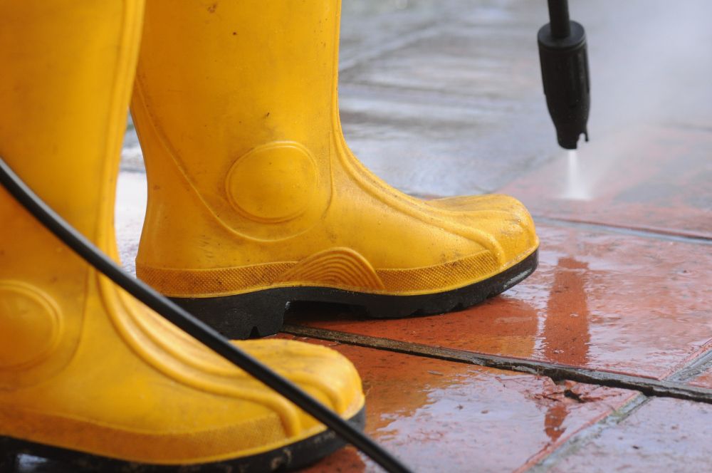 Worker using a high-pressure water nozzle to clean outdoor tiles