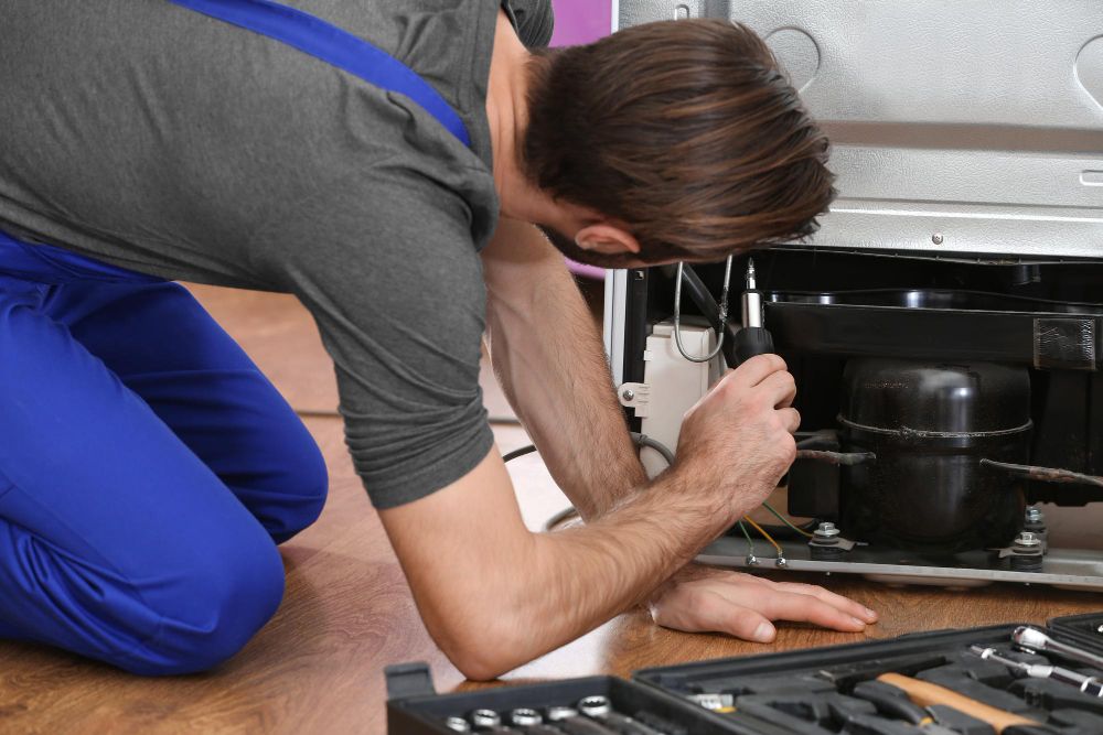 Appliance technician repairing a refrigerator with professional tools
