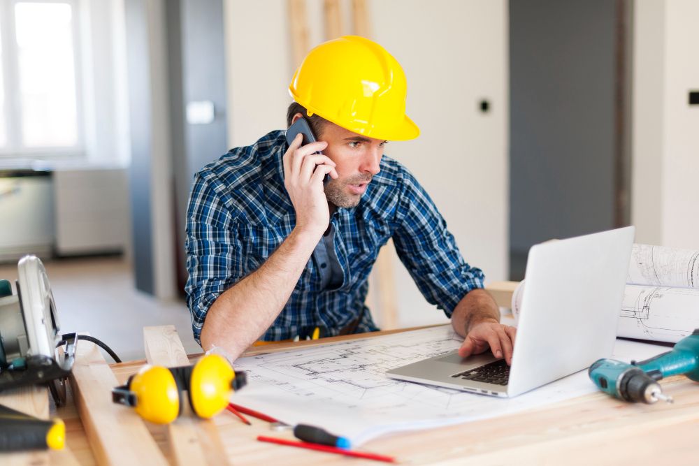 Construction professional using a laptop and phone on a job site